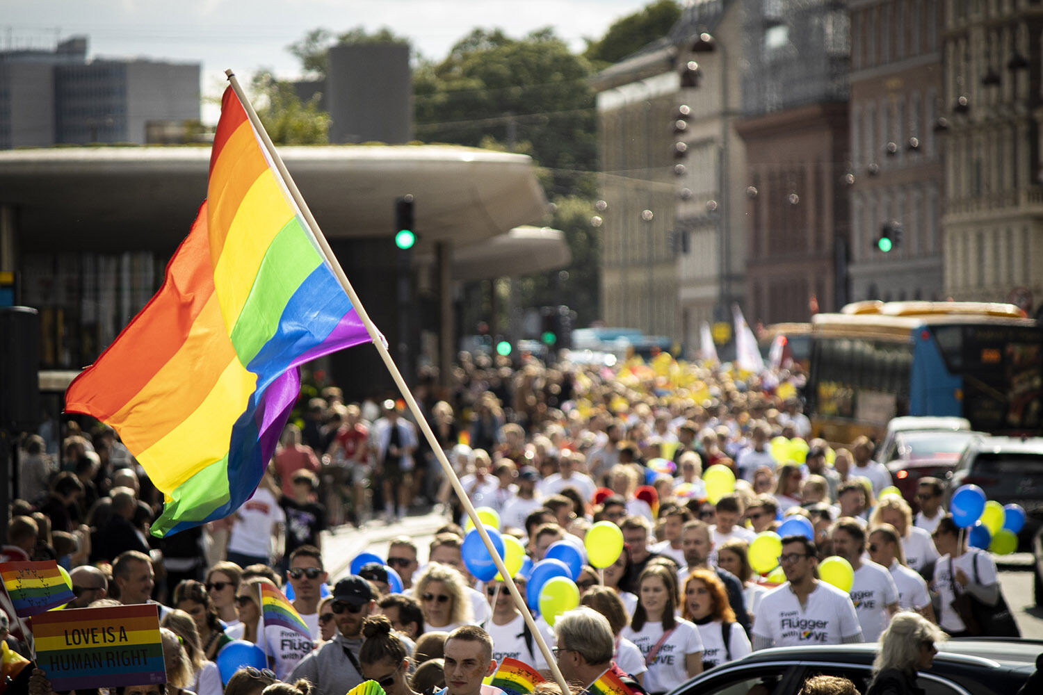 Lång demonstrationståg med en prideflagga i förgrunden